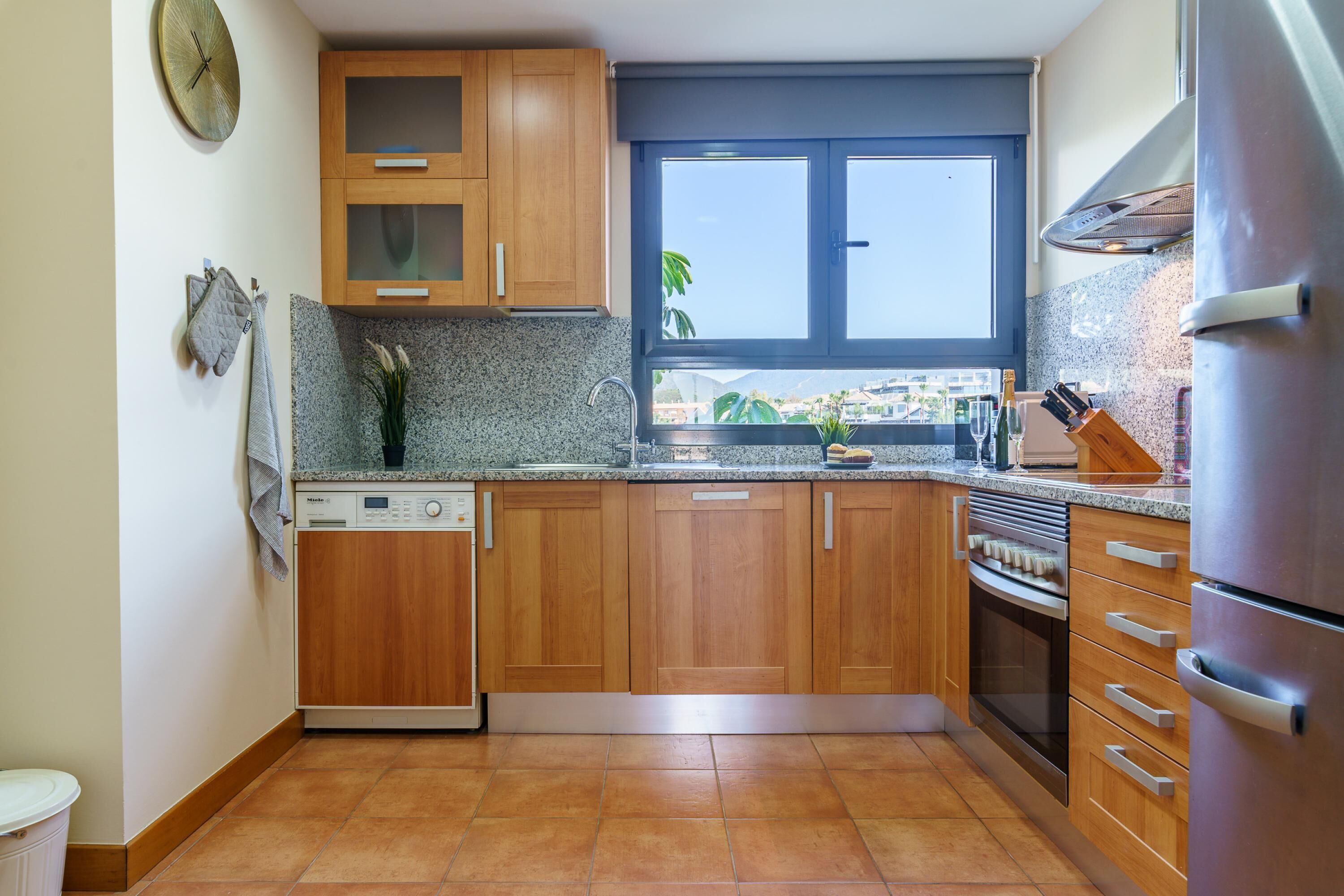 Una cocina con armarios de madera, horno empotrado, lavavajillas y ventana con vistas.