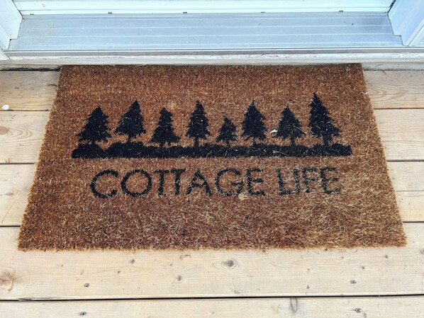 A brown doormat with a silhouette of trees and the words "COTTAGE LIFE" on a wooden floor.