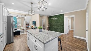 Una cocina moderna con encimeras de granito, armarios blancos y una pared verde con una cita.