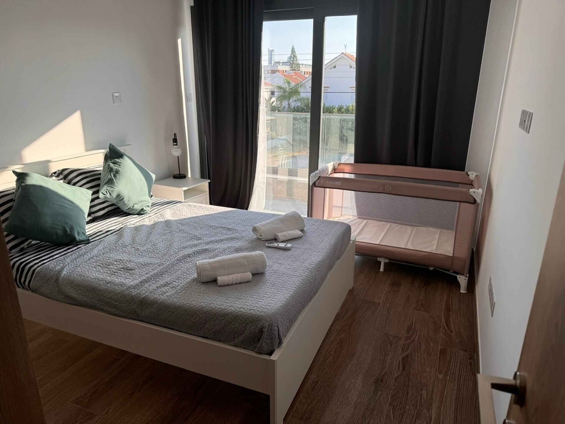 Un dormitorio moderno con una cama, una mesita de noche, cortinas y vistas a edificios.