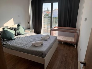 Ein modernes Schlafzimmer mit einem Bett, einem kleinen Nachttisch, Vorhängen vor einem Fenster und Blick auf Gebäude.