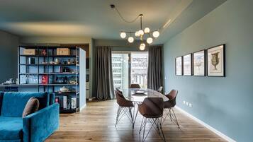 A modern living room with a dining table, blue sofa, and a bookshelf.