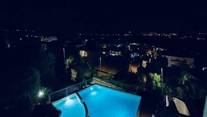 A nighttime view of a swimming pool with a surrounding fence, surrounded by trees and buildings. - Nicole House With Stunning View And Pool (Badesi)