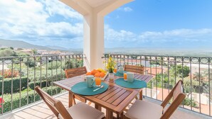A balcony with a wooden table and chairs, a view of the countryside, and a railing. - Nicole House With Stunning View And Pool (Badesi)