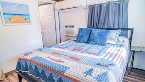 A bed with a quilt, a door, an air conditioning unit, and a picture on the wall.