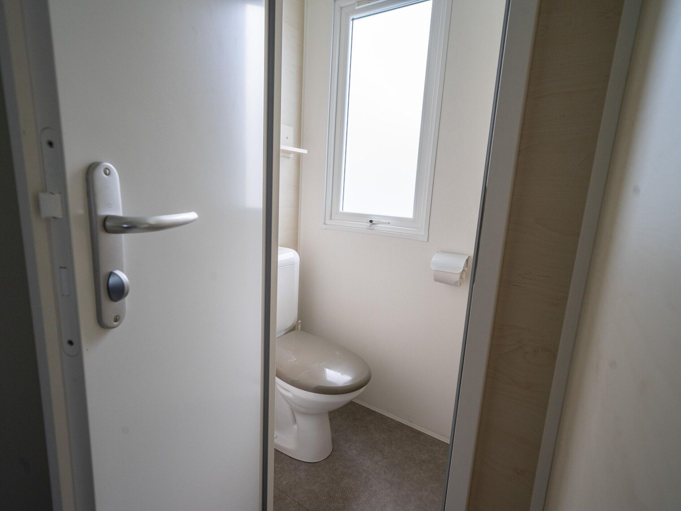 A bathroom with a toilet, a window, and a roll of toilet paper on the wall.