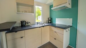 Cocina compacta con cubierta negra, armarios color beige, una ventana y una pared de acento color verde azulado.
