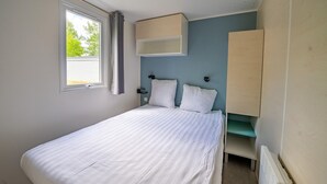 Un dormitorio con cama, ventana con cortinas, estante empotrado y radiador.