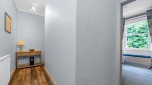 A hallway with wooden flooring, a small table with a lamp, and a window with a view of greenery.