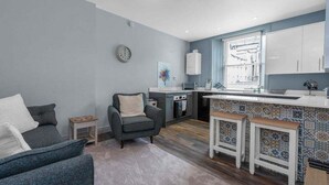 A compact living space with a kitchenette, a sofa, a chair, and a small table.