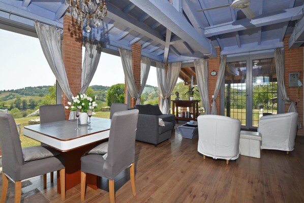 A spacious living area with a dining table, grey sofas, and a view of the countryside. - Villa Borgiano in Scansano (Scansano)
