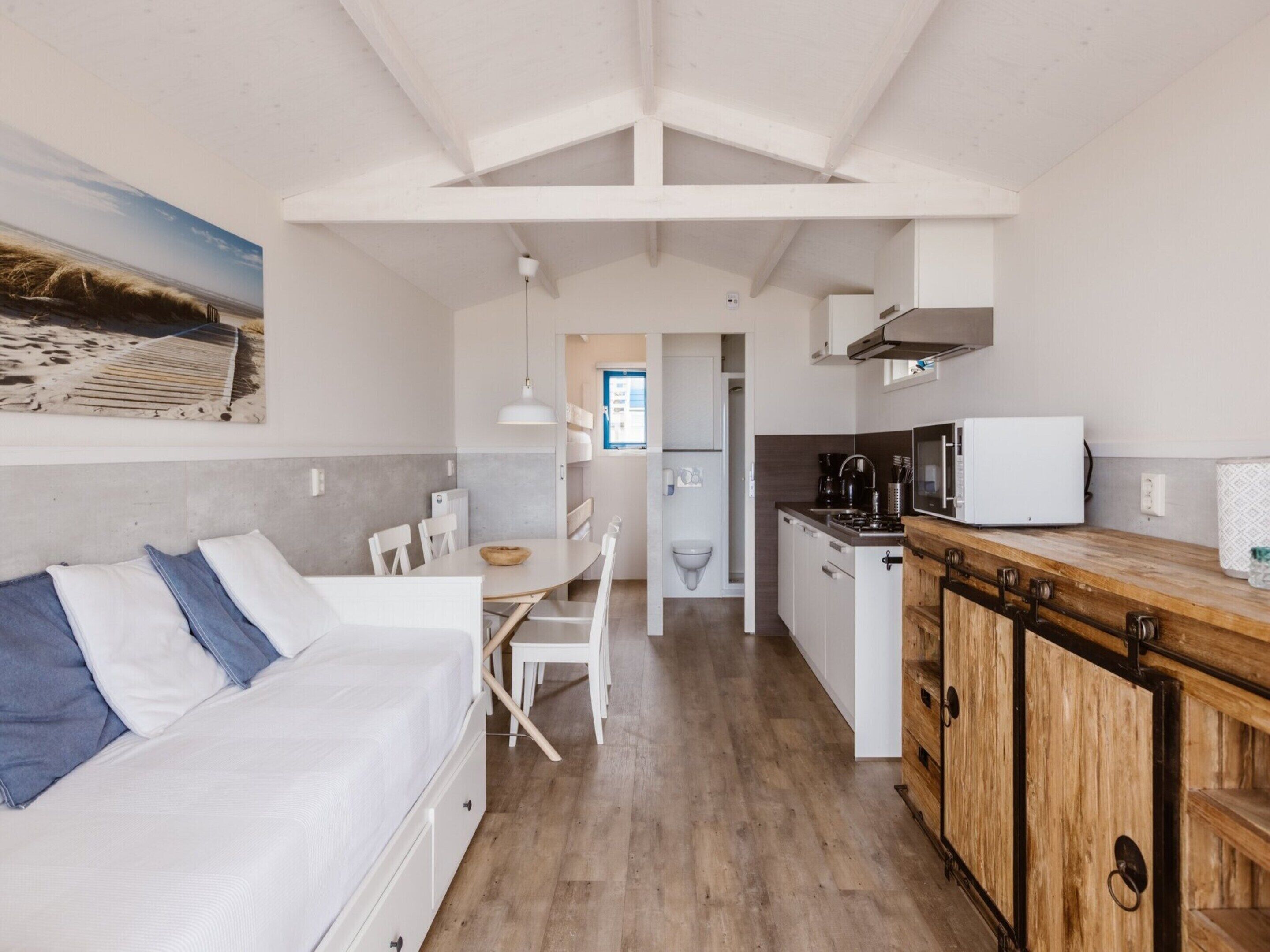 A compact, modern room with a bed, a dining table, and a kitchenette.
