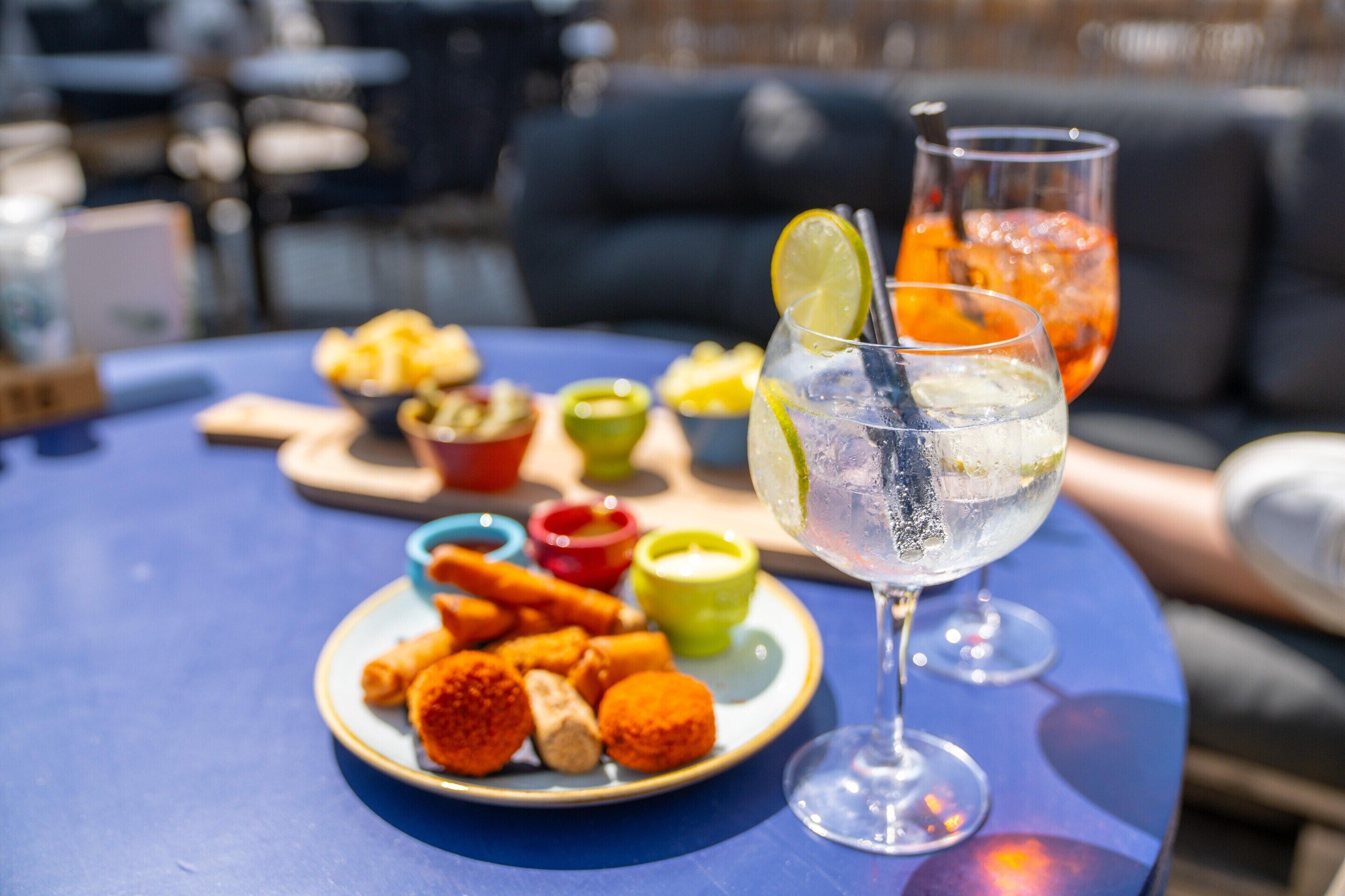 A table with a plate of snacks and a glass of iced drink, set on an outdoor table.