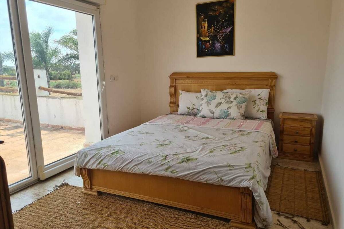 Ein Schlafzimmer mit Bett, Nachttisch, einem Gemälde und Blick durch eine Schiebetür.