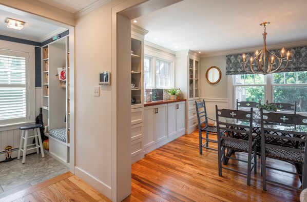 A kitchen with wooden flooring, white cabinets, a dining table with chairs, and a chandelier.