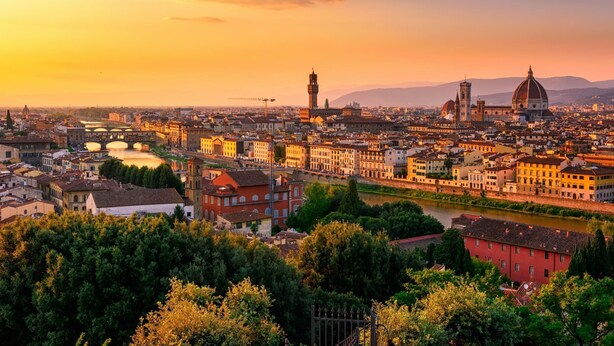 Ein weiter Blick über eine Stadtlandschaft mit markanter historischer Architektur, darunter Kuppelbauten und ein Turm, während der Sonnenuntergang.
