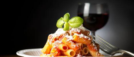 A plate of pasta with a glass of red wine in the background.