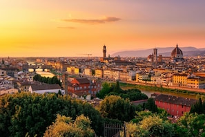 Ein weiter Blick über eine Stadtlandschaft mit markanter historischer Architektur, darunter Kuppelbauten und ein Turm, während der Sonnenuntergang.