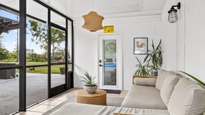 A modern interior with a large glass door leading outside, a wicker sofa, a small round table with a plant, and a framed picture on the wall.