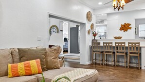 A living room with a sofa, a dining area with a table and chairs, and a kitchen in the background.