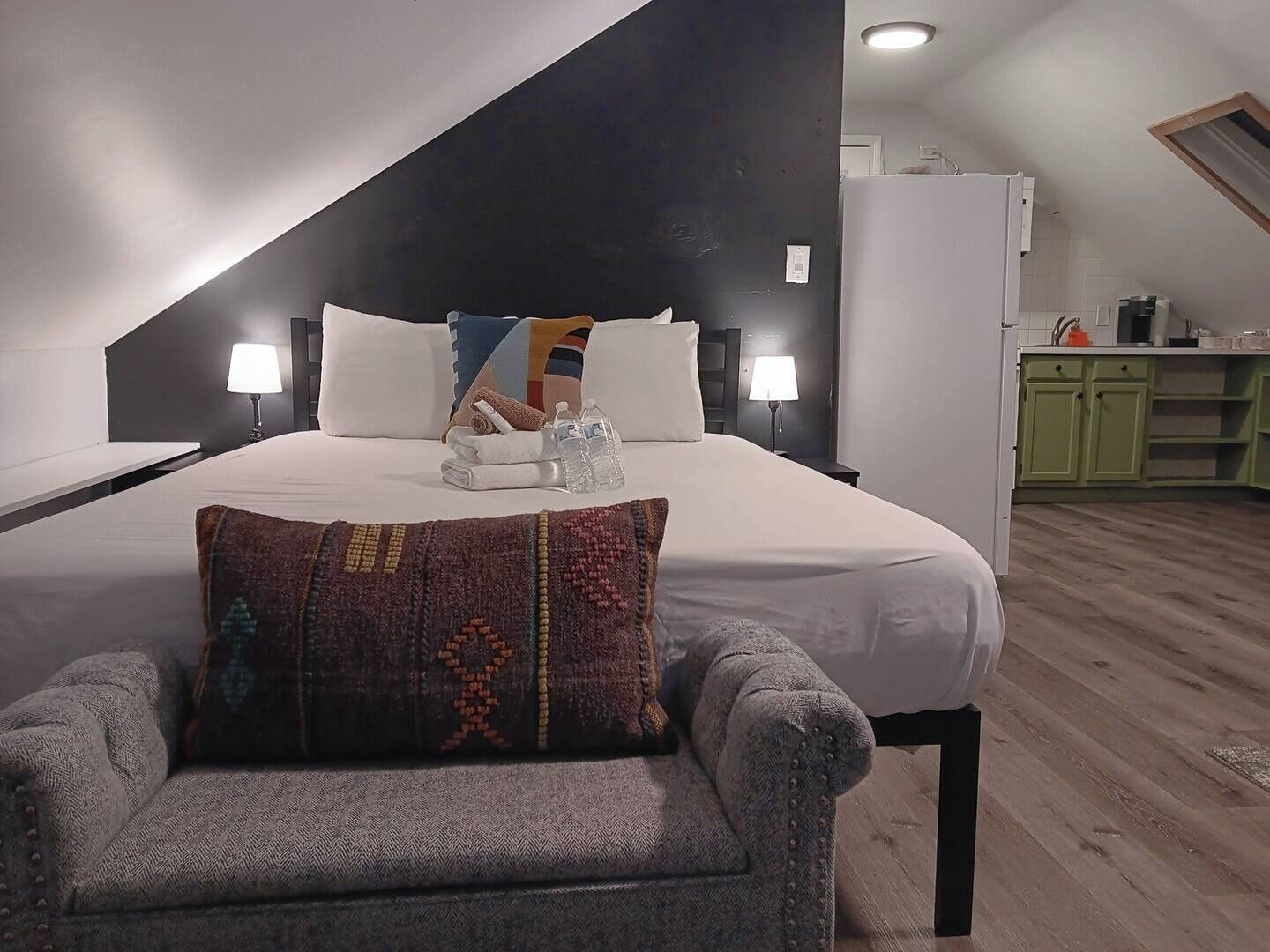 A modern bedroom with a large bed, two bedside lamps, a colorful pillow, and a small armchair.