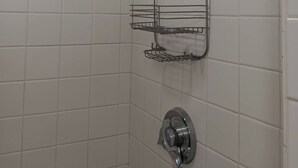Ducha con cabezal de ducha de mano y estante adosado a la pared.