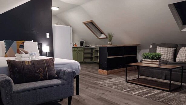 Un dormitorio moderno estilo loft con cama, un sillón gris, una mesita de café y una estantería empotrada para la televisión.