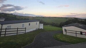 A caravan park with a paved driveway leading to a white caravan with a fenced area. - Ty-dee Holiday Home Inside Polperro Holiday (Looe)