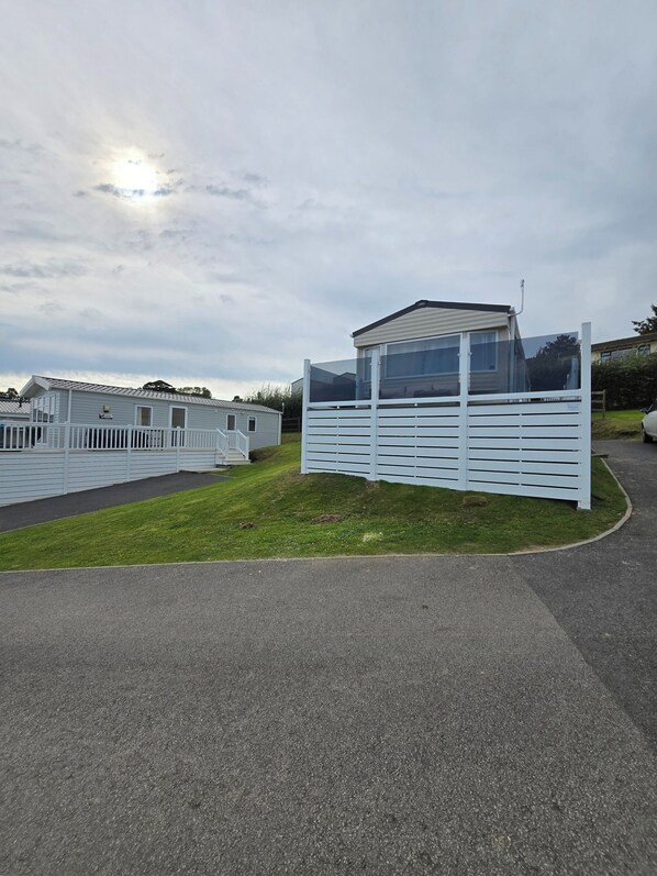 A caravan park with a fenced area, a grassy lawn, and a paved road. - Ty-dee Holiday Home Inside Polperro Holiday (Looe)