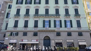A multi-story building with a central entrance, storefronts on the ground floor, and a row of windows with shutters.