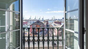 A view from a balcony with a metal railing, overlooking a harbor with cranes and buildings.