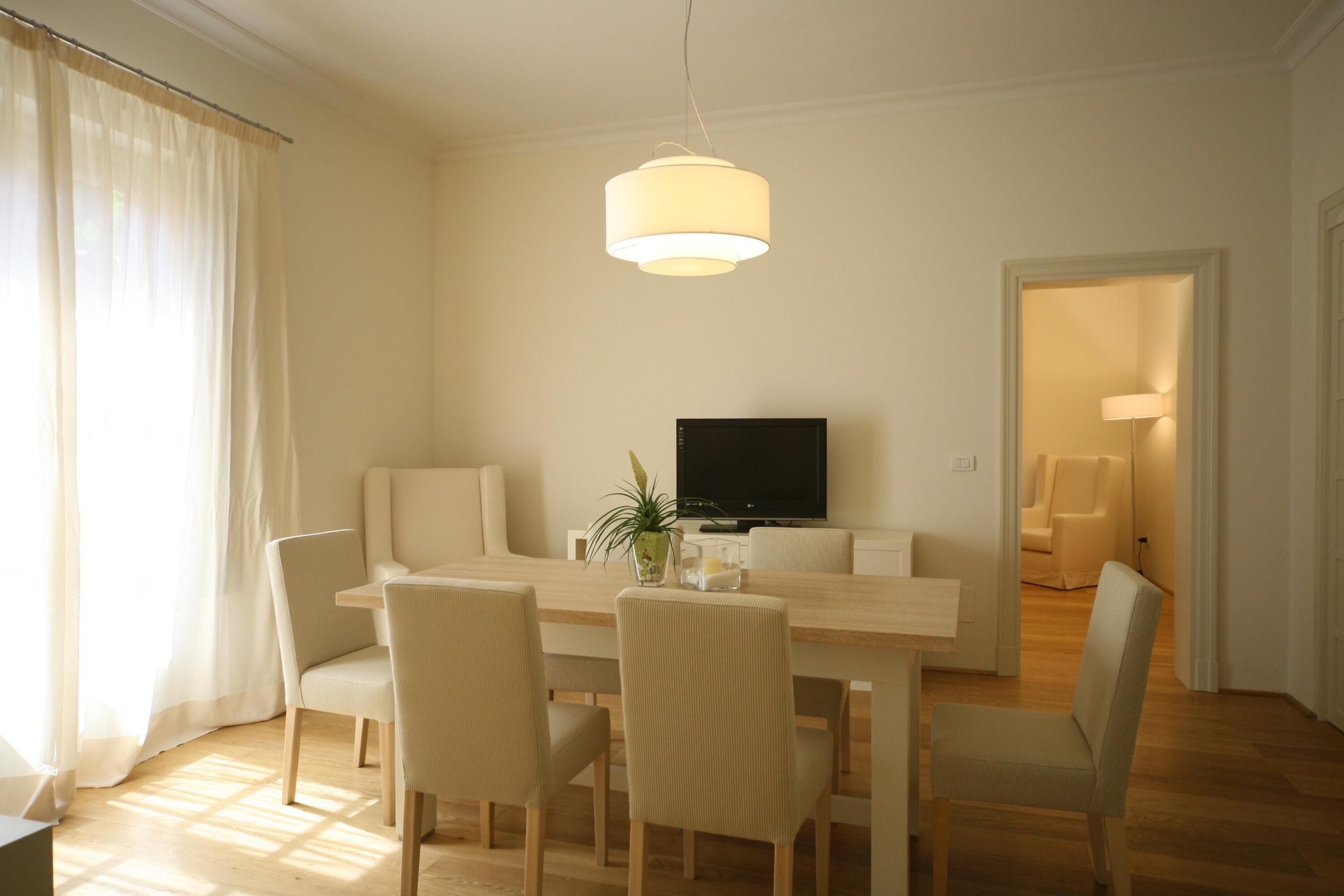 Un coin repas comprenant une table en bois, quatre chaises, un téléviseur et un luminaire suspendu.