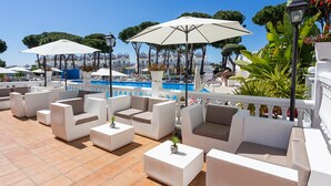 Un espace piscine sur le toit, avec des meubles d’extérieur blancs, des parasols et une vue dégagée sur la piscine.