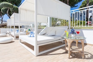 Relax in a serene outdoor lounge with a cushioned bench and glass-top table, surrounded by lush greenery.
