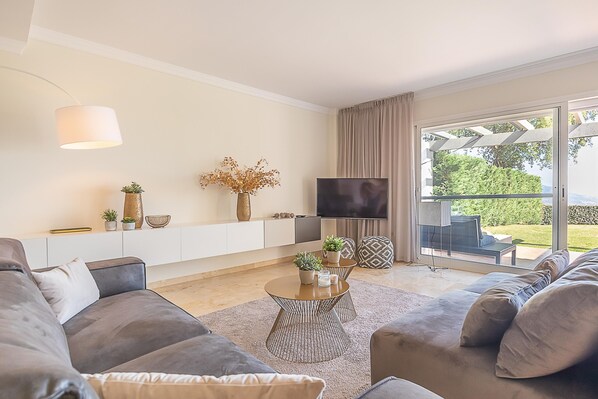 A modern living room with a sofa set, a coffee table, a TV, and a view of the outdoors. - Apt Mairena Forest sea View Pool (Ojén)