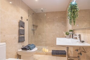 A modern bathroom with a glass-enclosed shower, a toilet, a sink with a mirror, and a hanging plant.