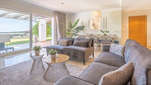 Ein modernes Wohnzimmer mit einer Couch, einem Couchtisch und Topfpflanzen. Es gibt einen Essbereich mit Stühlen und einem Tisch.