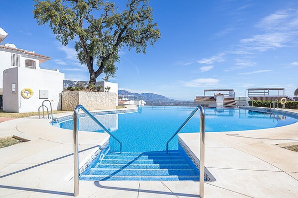 A swimming pool with steps leading into it, surrounded by a white building and a large tree.