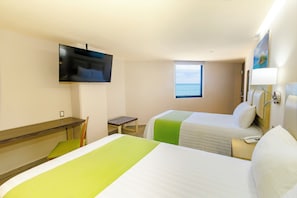 Habitación de hotel con dos camas, televisor montado en la pared, ventana con vista al mar y un escritorio con una silla.