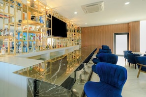 Zona de bar con encimera de mármol, estanterías con botellas, un televisor de pantalla plana y sillones tapizados en azul.