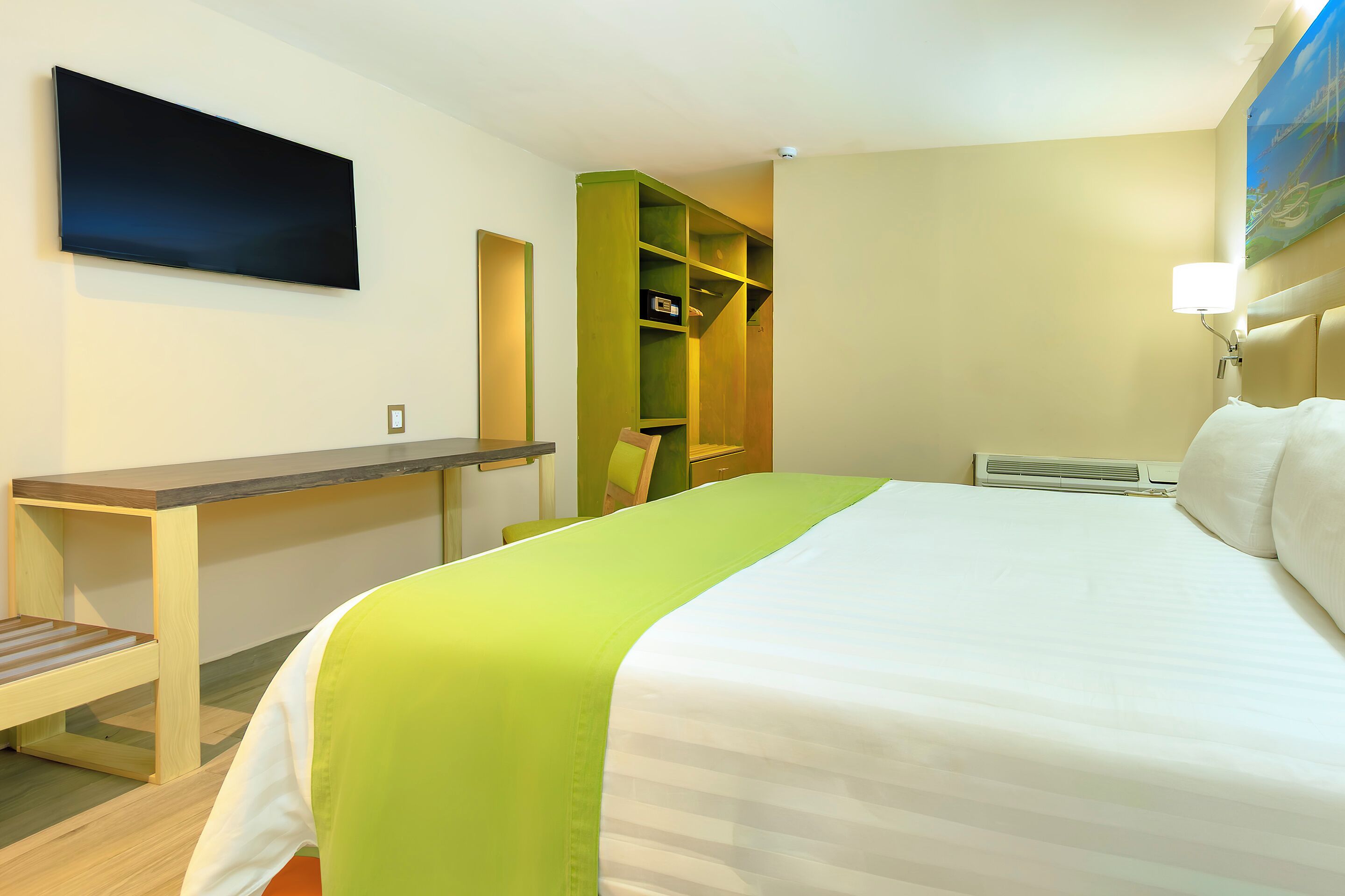 A hotel room with a bed, a desk, a chair, a wardrobe, and a painting on the wall.