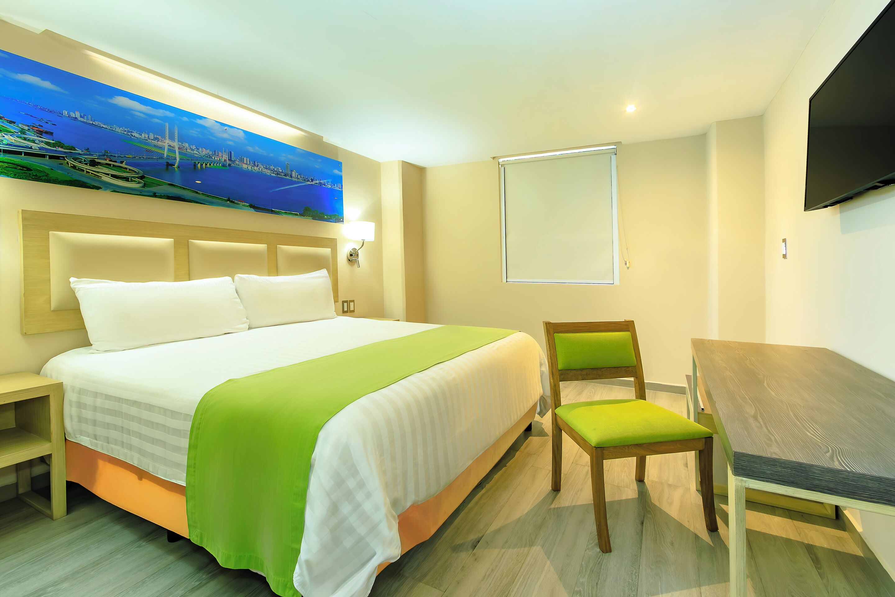 A hotel room with a bed, a desk, a chair, a TV, and a painting on the wall.