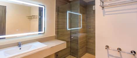 Un baño moderno con cabina de ducha de vidrio, un espejo grande con iluminación LED y un perchero de toallas cromado.