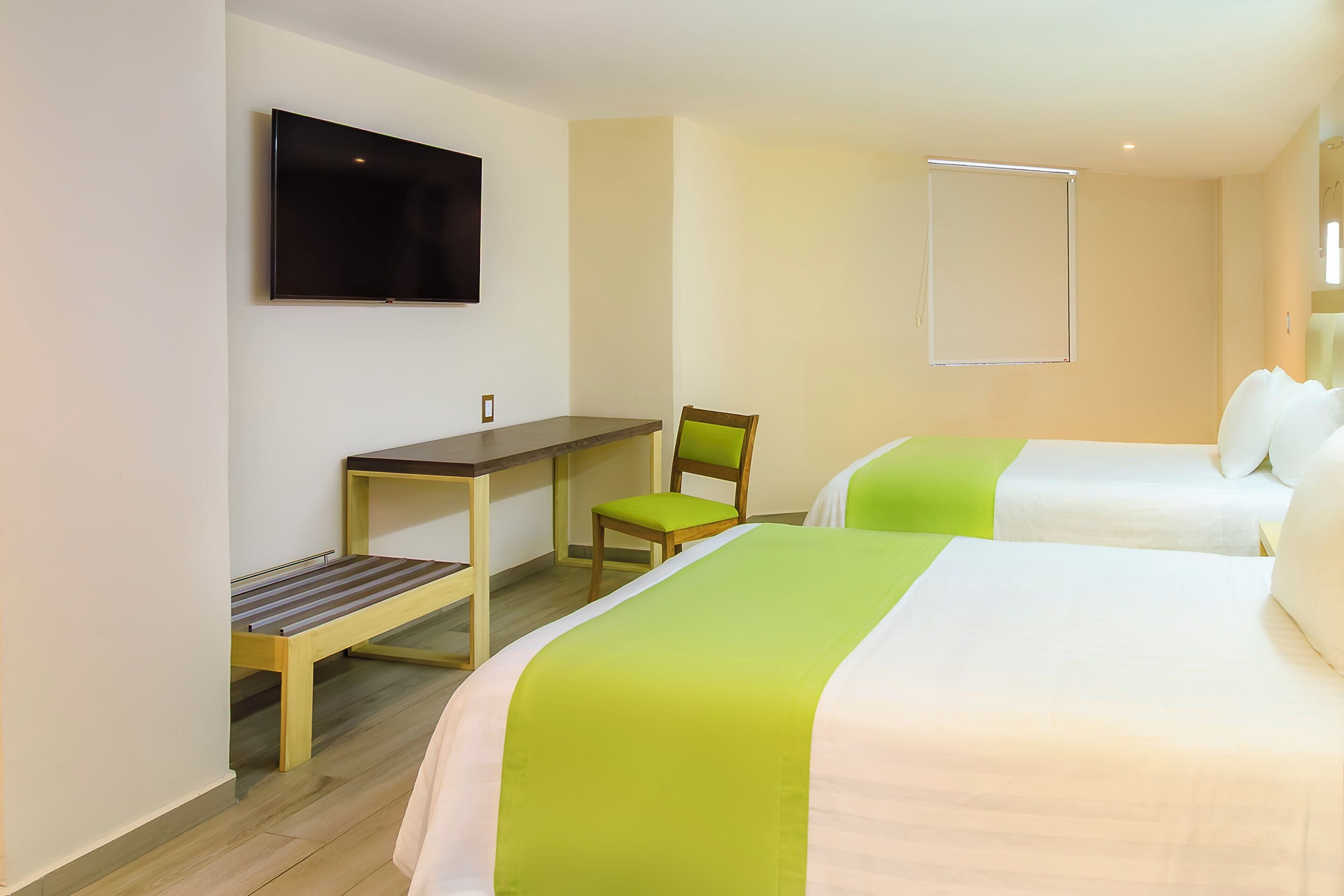 A hotel room with two beds, a desk, a chair, a TV, and a window.