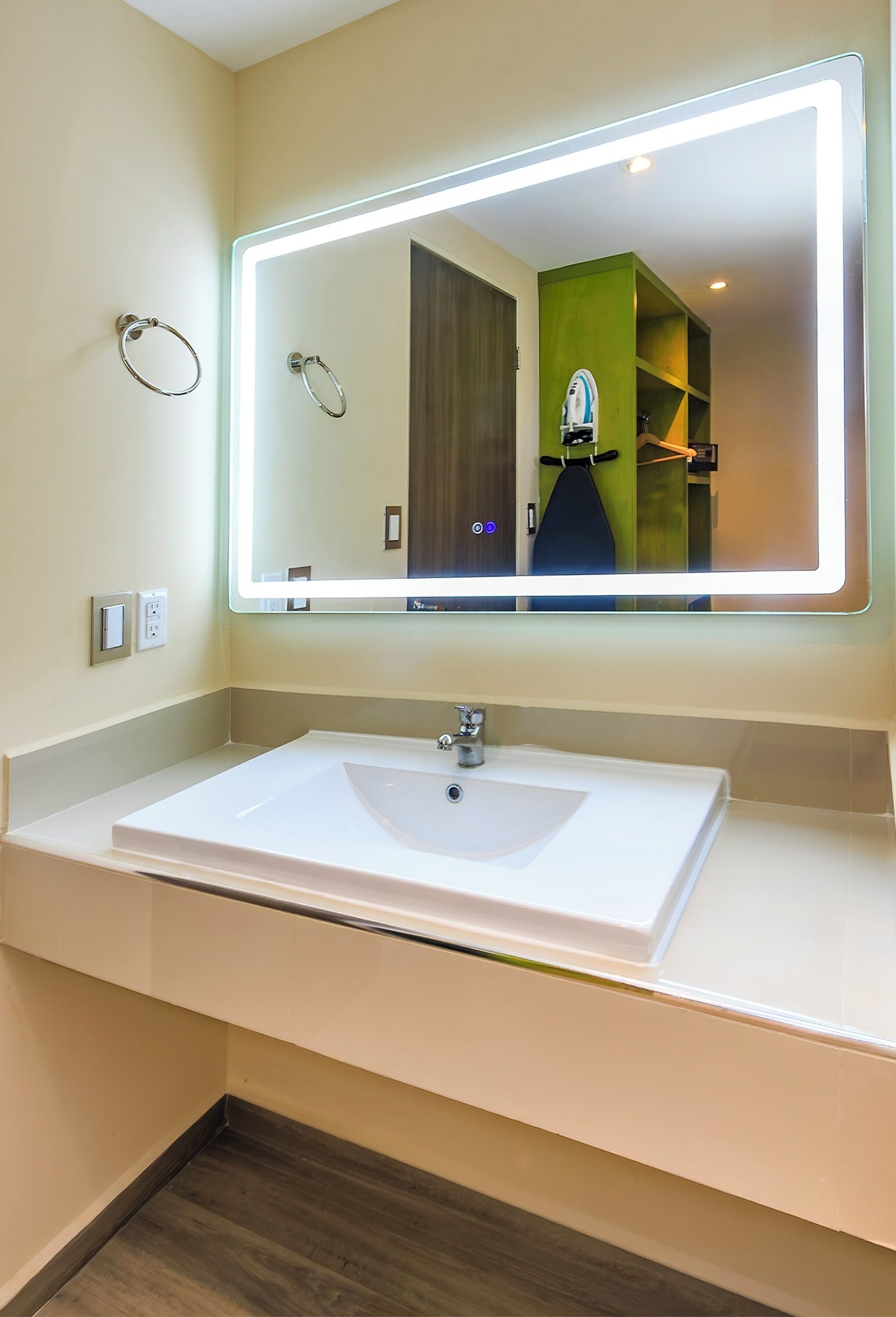 Un baño moderno con un espejo grande, un lavabo blanco y una pared de acento verde.