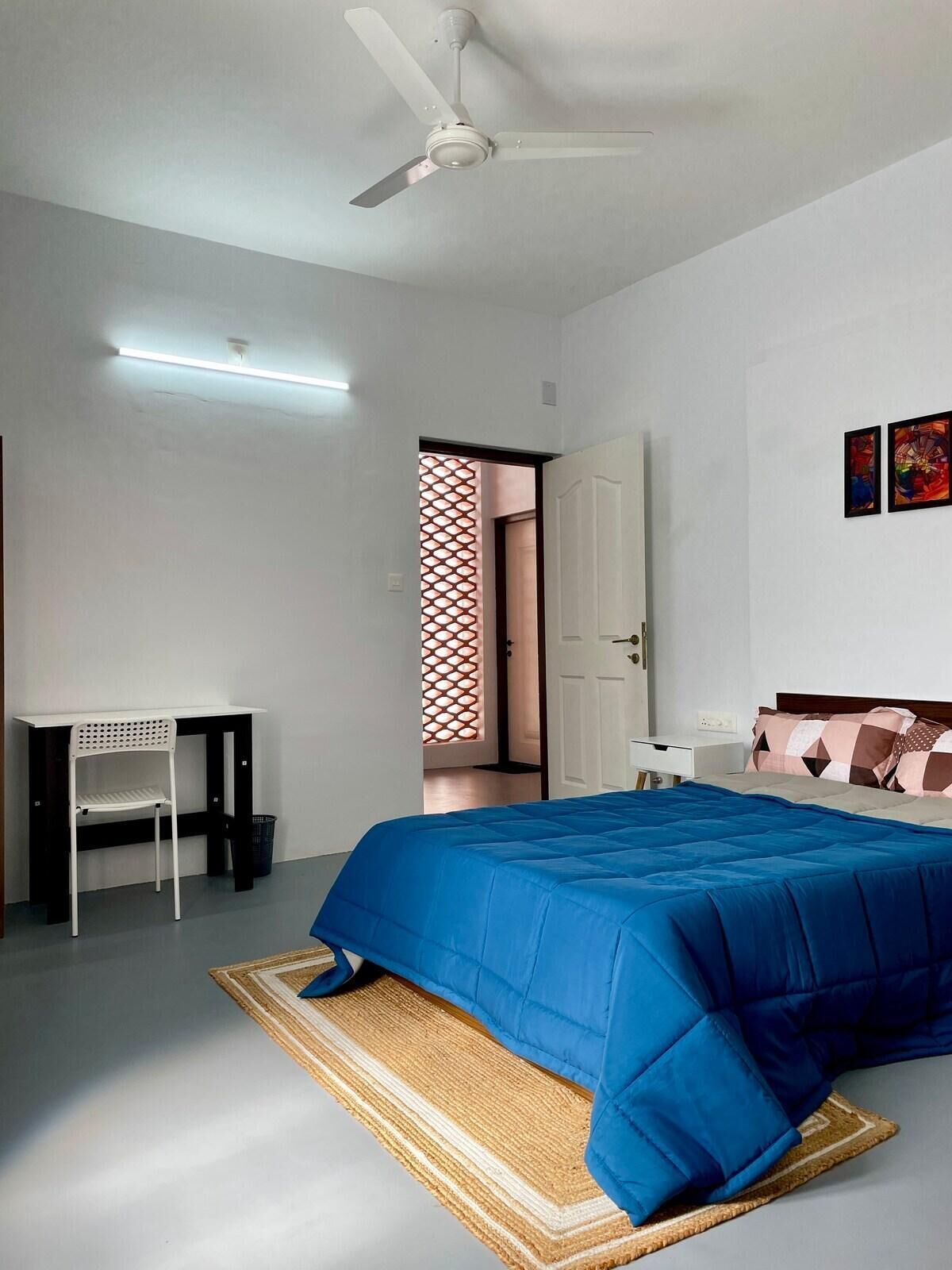 A bedroom with a bed, a desk, a chair, and a ceiling fan.