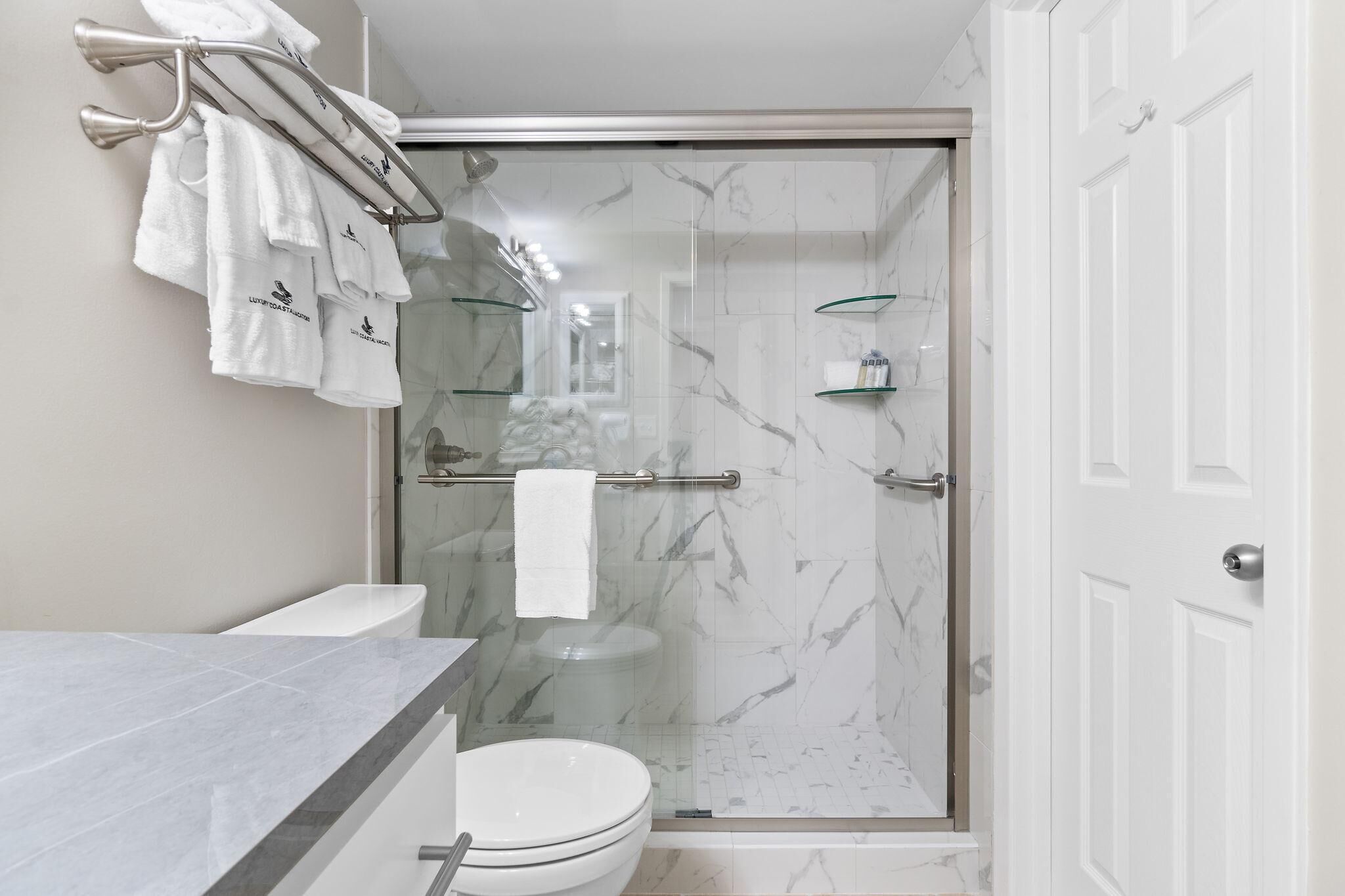 Et moderne badeværelse med et glasafskærmet brusebad, toilet og et håndvaskbord med marmorplade.