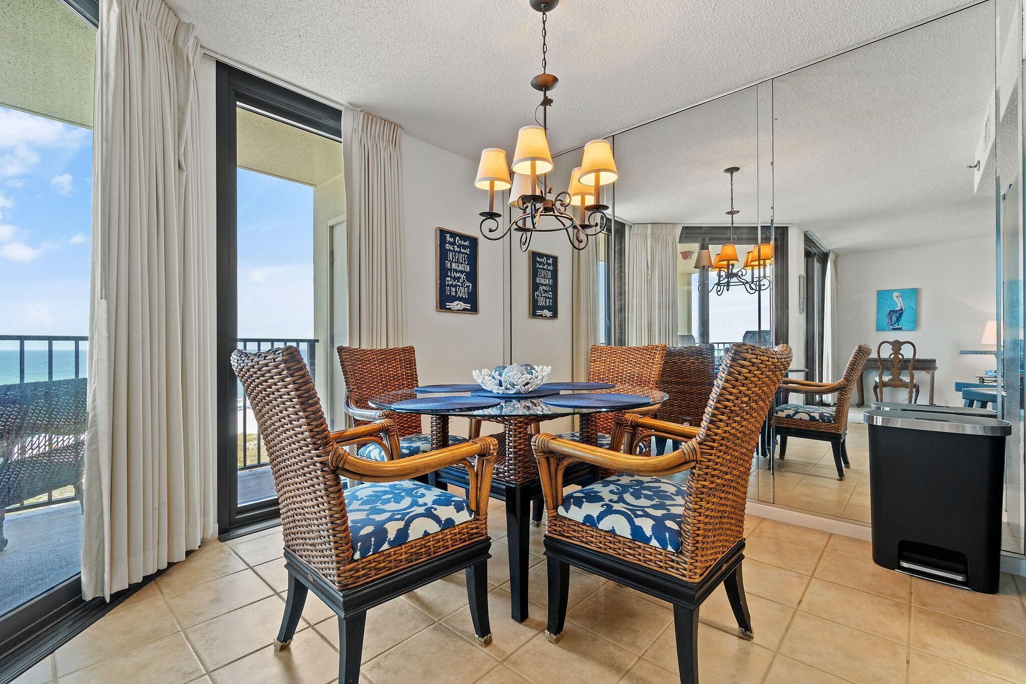 Un coin repas avec des chaises en osier et une table, un lustre et une vue sur l’océan.