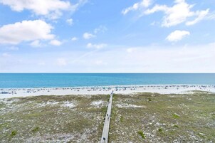 A beach with a long pier extending into the ocean, surrounded by sandy areas with people and beach umbrellas.