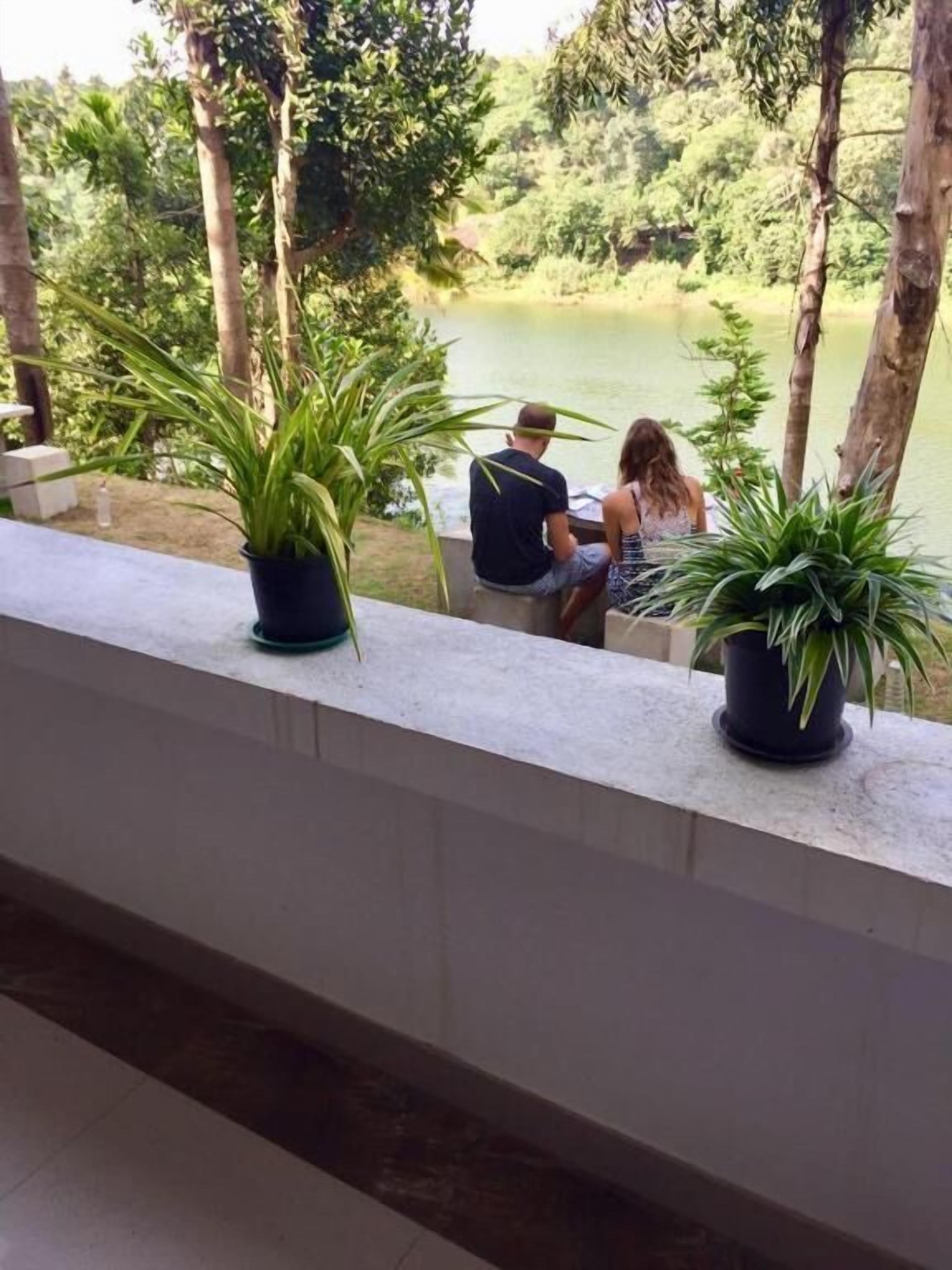 Una coppia seduta su un balcone con vista su un corpo d'acqua, con piante in vaso sulla ringhiera.